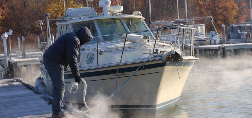 How to winterize a boat: person cleaning and washing down a white cruiser boat with high-pressure hose on a misty fall day at the marina