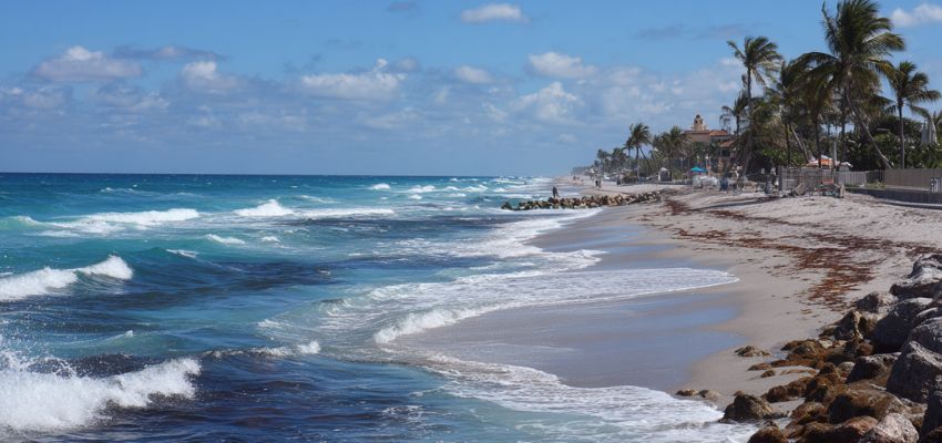 Waves rolling onto a wide sandy beach lined with palms and rocks in Boca Raton, capturing relaxing beach days as one of the top things to do Boca Raton